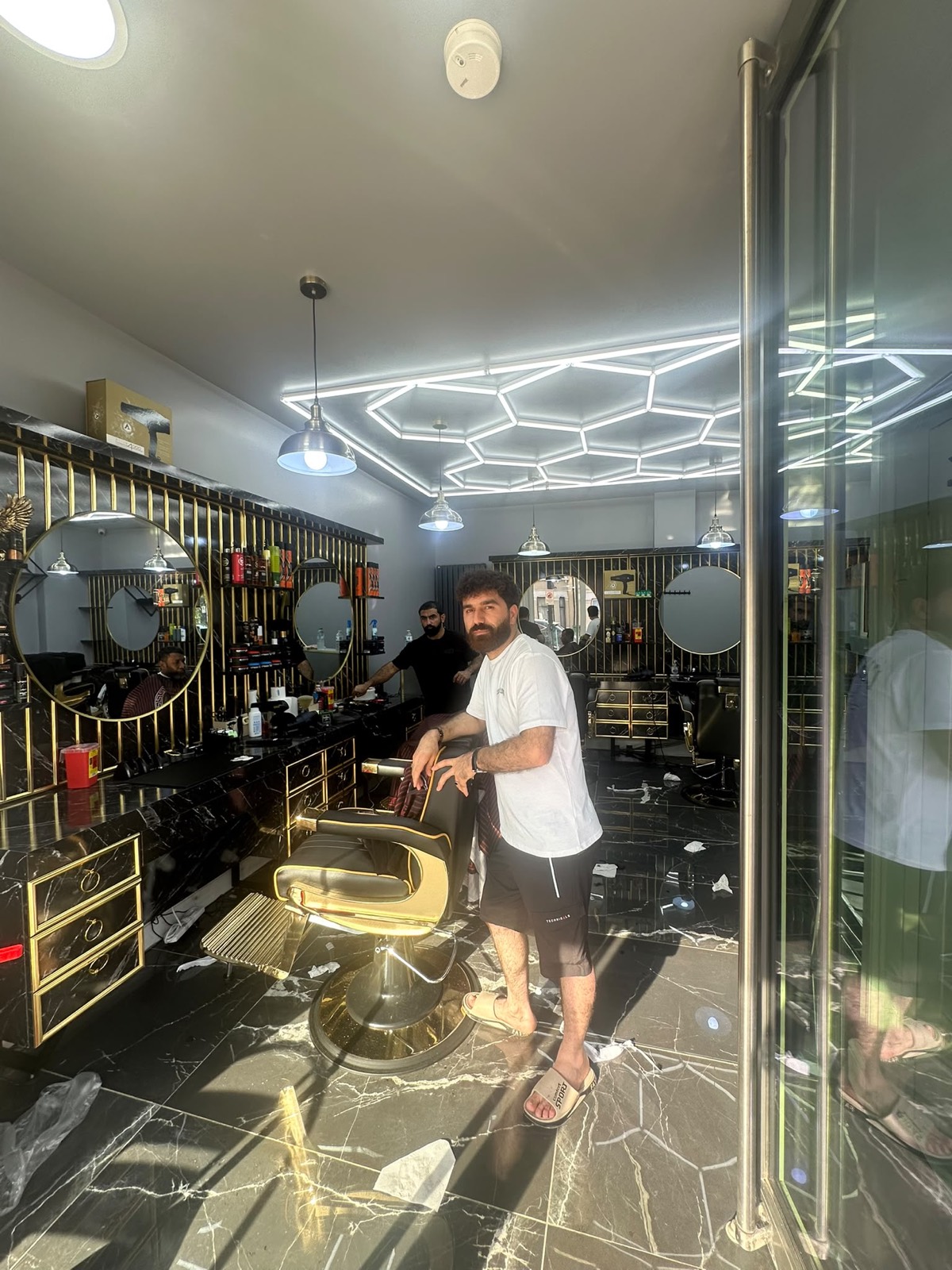 Barber by the styling chair under hexagon lights